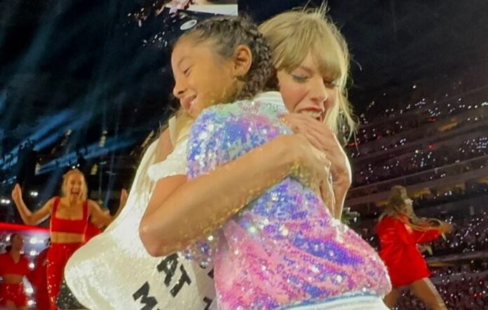 Taylor Swift trots up to a young fan belting out her song lyrics. After giving the girl a sweet hug, Swift hands her the coveted 22 trilby, causing the young fan to burst into happy tears...